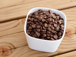 White bowl with roasted coffee beans on wooden table