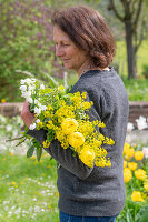 Frau hält Blumenstrauß mit Traubenkirsche, Raps, Sommerknotenblume (Leucojum aestivum) 'Gravetye Giant', Tulpe 'Strong Gold' (Tulipa) und Wollziest