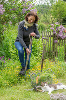 Woman cutting out Ranunculus acris, cat next to her