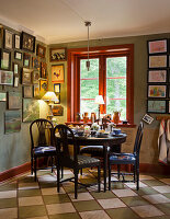 Dining area with round wooden table, picture gallery on green wall and red window frame