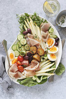 Salad platter with white asparagus, prosciutto, fried potatoes, eggs and vegetables