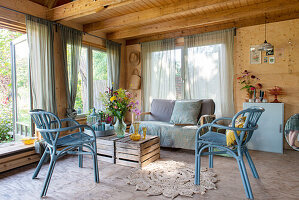 Summer garden shed with blue rattan chairs, wooden table and bouquet of flowers