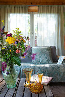 Bouquet of flowers in glass vase and vintage sofa in front of window with transparent curtains