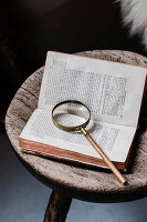 Old book and magnifying glass on wooden stool