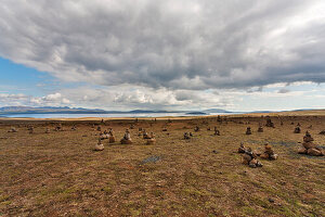 Steinhaufen auf einem Feld mit See und Bergen im Hintergrund, Thingvellir, Island