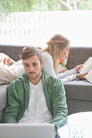 Man Using Laptop and Woman Reading Book on Sofa