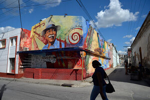 Cuba,santiago,a woman is walking in front of a large colorful painting made on a building walls