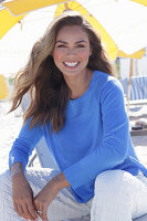 Woman in blue jumper and white trousers sitting on the beach