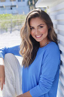 Frau in blauem Pullover und weißer Hose auf Veranda sitzend