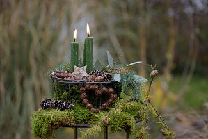 Decorated metal basket with moss, cones and green candles in the garden