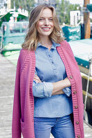 Junge Frau im Jeans-Outfit und rosa Strickjacke am Hafen