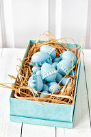 Light blue Easter eggs decorated with lace ribbon in a turquoise box on a wooden table