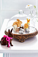 Decorative rabbit figurines under a glass bell on a wooden plinth