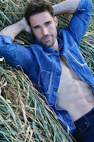 Person in denim shirt and jeans, lying in the hay