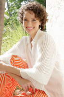 Brunette woman in cream-coloured blouse and orange-coloured patterned trousers