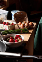 Frische Eier, Erdbeeren und Schnittlauch liegen auf Holztisch