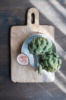 Two raw artichokes with pink salt on a chopping board