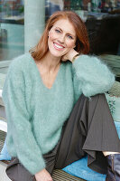 Rothaarige Frau in mintfarbenem Strickpullover und grauer Hose