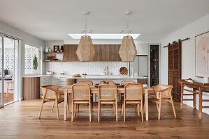 Dining area with wooden table and modern pendant lights, open kitchen in the background