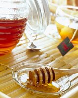 Honiglöffel neben Honigtopf, Teetasse im Hintergrund