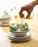 Hand giesst Öl auf Salat