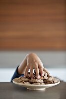 Child's hand stealing a cookie from a plate of cookies