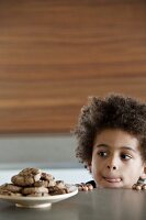 Young boy licking his lips infront of a plate of delicious cookies