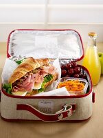 Croissant-Sandwich mit Möhrenrohkost und Trauben in Lunch-Koffer