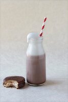Bottle of chocolate milk with a straw and a bitten biscuit