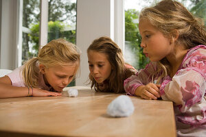 Drei Mädchen spielen Wattebausch blasen, Kindergeburtstag