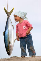 A little girl stands on the beach and next to a hanging yellowtail, Punta Conejo, Baja California Sur, Mexico, America