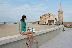 Woman sitting on a wall at Madonna dell' Angelo church, Caorle, Venice, Veneto, Italy