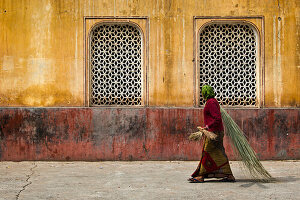 Woman with bamboo brushes in front of a building in the Galtaji temple, Jaipur, Rajasthan, India