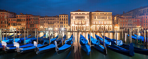 Panorama mit Blick über den Canal Grande mit den beleuchteten Fassaden des Palazzo Ca' Loredan und des Palazzo Ca' Farsetti (von links) im Blau der Nacht und Gondeln im Vordergrund, San Marco, Venedig, Venezien, Italien