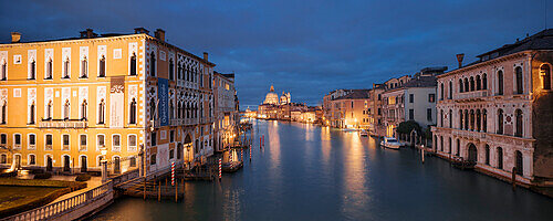 Panorama mit Blick von der Ponte dell'Accademia über den Canal Grande mit beleuchteten Häusern, dem Palazzo Cavalli-Franchetti links, dem Palazzo Contarini Polignac rechts und der Kirche Santa Maria della Salute im Hintergrund im Blau der Nacht, Dorsoduro