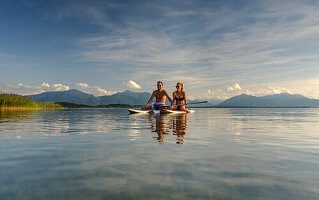 A young couple on their SUP boards on the Chiemsee, in the background the Chiemgau Alps, Chieming, Upper Bavaria, Germany