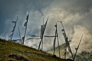 Gebetsfahnen zum Gedenken an einen Verstorbenen, mit dem Mantra Om Mani Padme hum bedruckt, mit dunklen Wolken und Bergen im, Phobjikha Tal, Bhutan, Himalaya, Asien