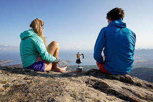 Zwei junge Menschen kochen auf einem Gaskocher Kaffee mit Aussicht auf die Stadt Calvi und das Meer, Korsika