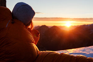 Frau in Daunenschlafsack blickt der aufgehenden Morgensonne entgegen, Gramai, Karwendel, Tirol, Österreich