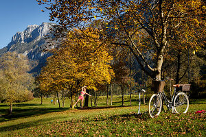 Junge Frau auf einer Slackline, die zwischen herbstlich gefärbten Bäumen gespannt ist, Kiefersfelden, Bayern, Deutschland