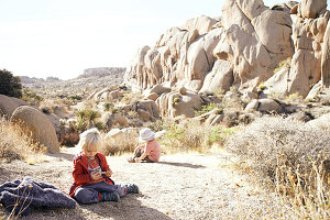 Kinder spielen auf einem Felsen vor der Kulisse der Jumbo Rocks im Joshua Tree Park, Kalifornien, USA