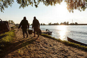 Danube Delta, an old couple carries shopping along the riverside path in the evening sun, Mila 23, Tulcea, Romania.