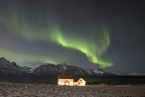 The typical house illuminated by lights and Northern Lights, Lyngen Alps, Tromso, Norway, Europe
