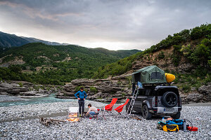 Albania, Southern Europe, young couple in front of off-road vehicle with roof tent, campfire, river, Vjosa, Permet