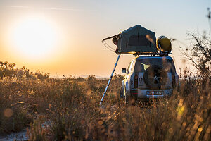 Albania, Southern Europe, young man looks out of the roof tent on an off-road vehicle in the evening sun