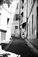 Schwarz-Weiß-Foto einer Frau, die an einem heißen Sommertag in Arles, Frankreich, eine Straße entlang geht.