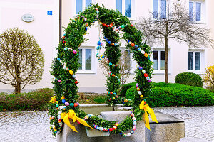  Easter fountain decorated with garlands of boxwood branches and colorful Easter eggs in front of the Old School in Forstinning in Upper Bavaria in Germany 