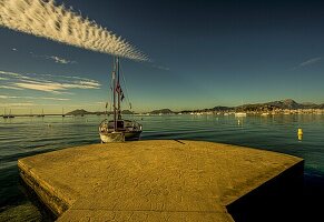 Traditionelles Segelboot (Llaüt) am Bootssteg, Blick über das Meer auf Port de Pollenca und das Tramuntana-Gebirge, Mallorca, Spanien