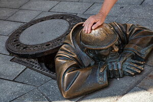 Hand berührt Cumil, eine Bronzeskulptur eines Mannes bei der Arbeit in einem Gulli, Bratislava, Slowakei, Europa