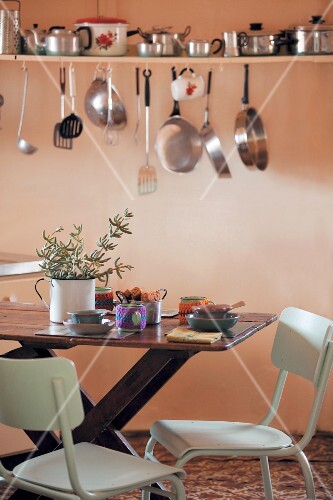 Pots Pans And Kitchen Utensils On Wall Mounted Shelf Above Dining Table In Pots Pans And Kitchen Utensils On Wall Mounted Shelf Above Dining Table In
